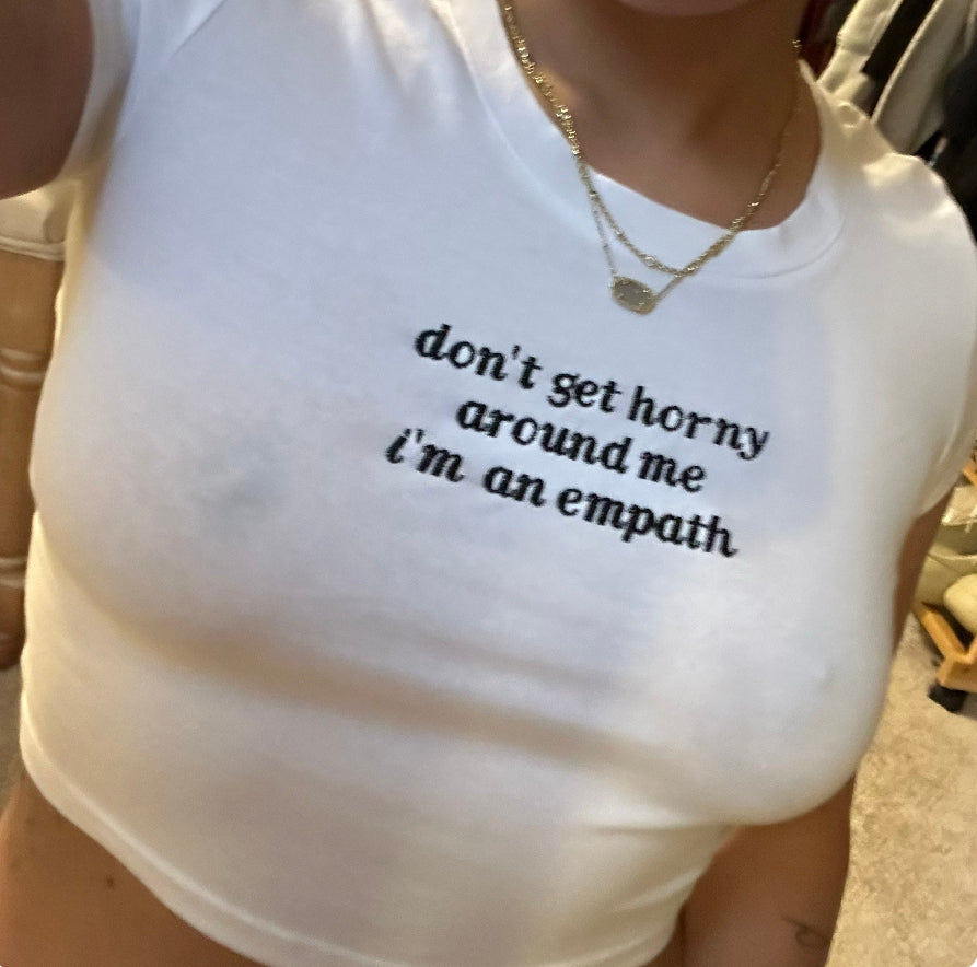 A person wearing a white t-shirt with the text "don't get horny around me I'm an empathy" printed on it.
