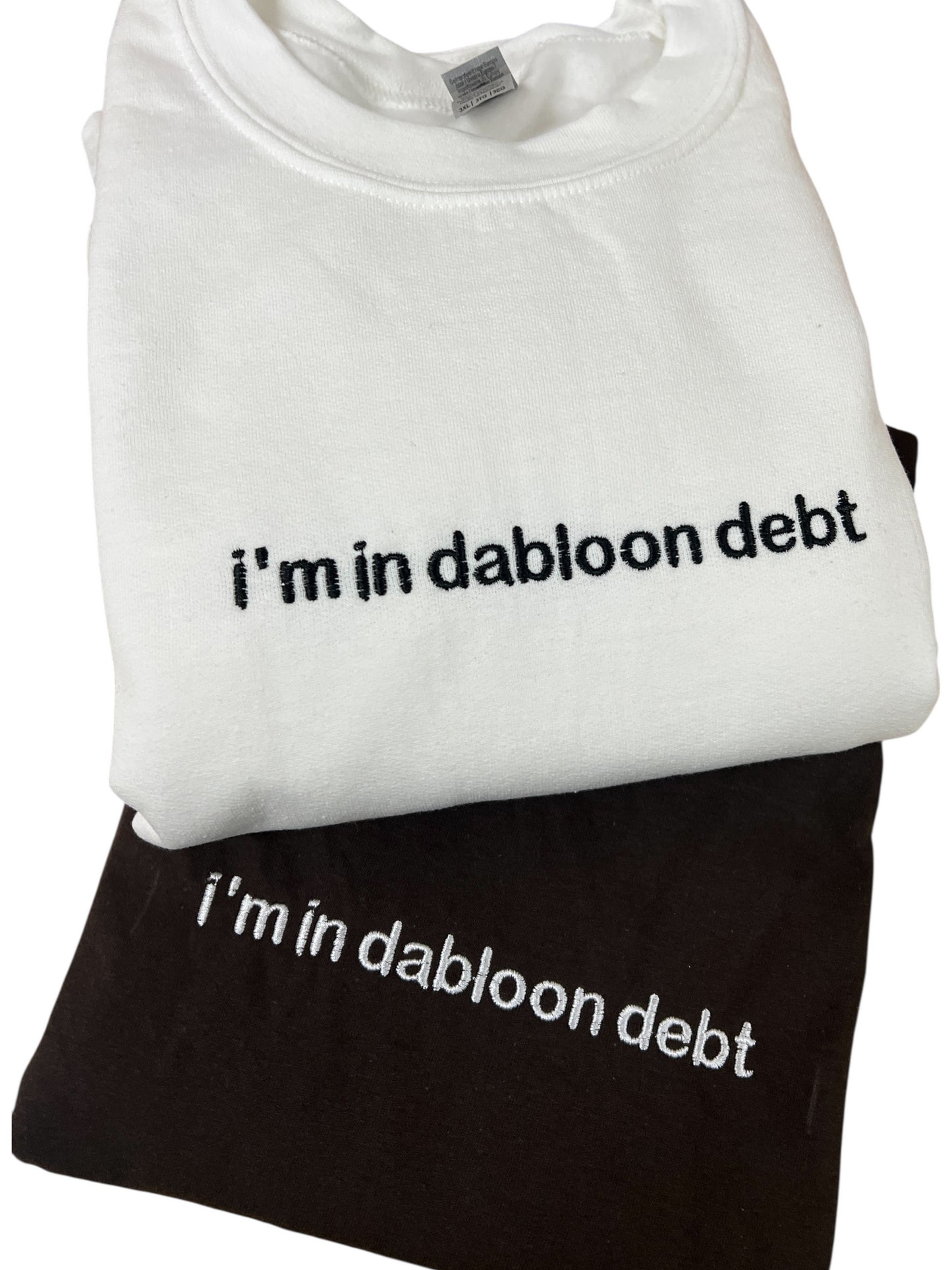 A white t-shirt with the text "i'm in dabloon debt" printed on it, and a black t-shirt underneath it.