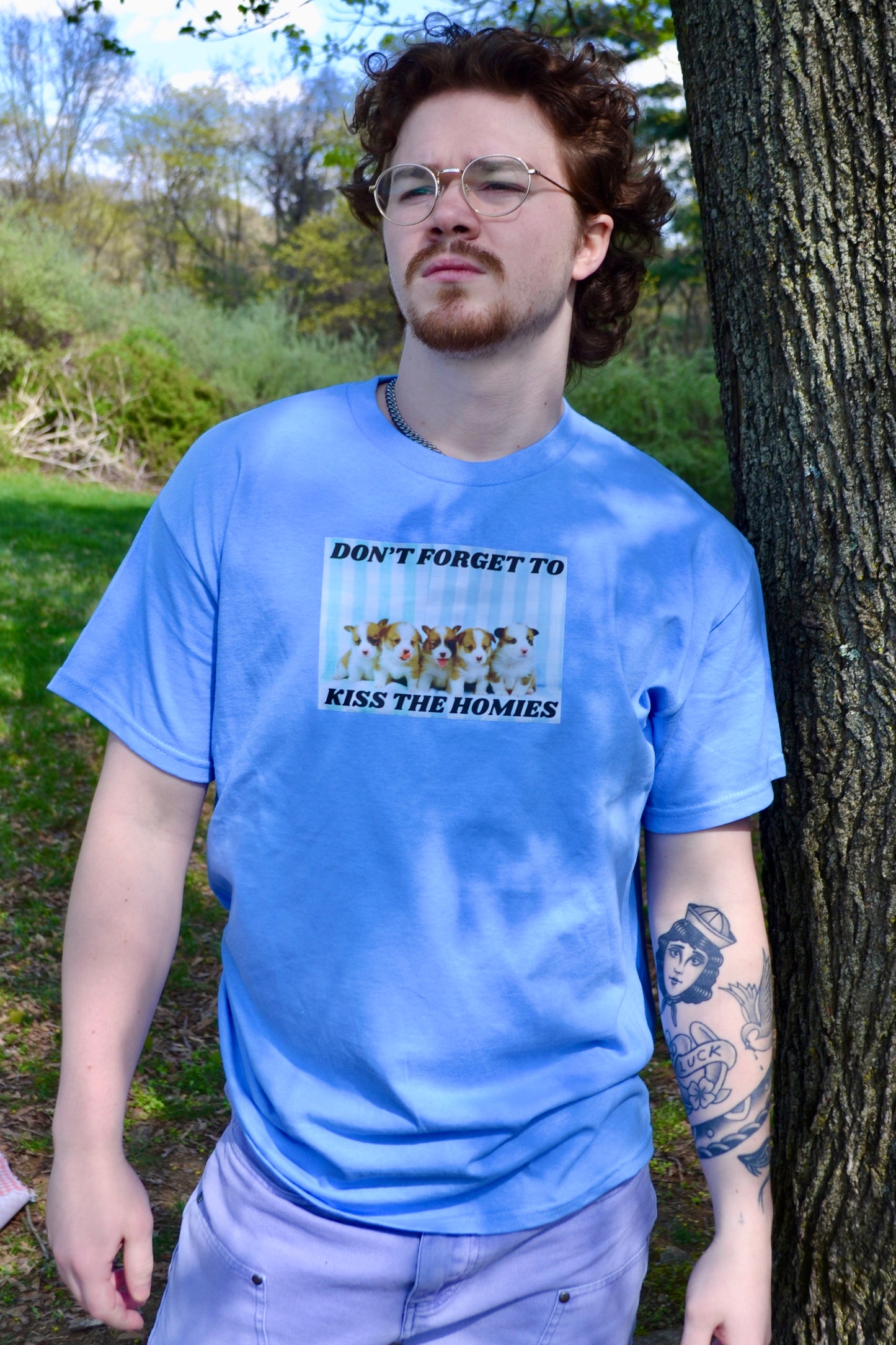 a man standing next to a tree wearing a blue shirt