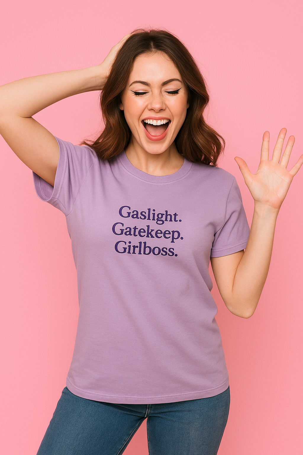 A woman wearing a purple t-shirt with the text "Gaslight. Gatekeeper. Girl boss." is smiling and waving with her hand raised.