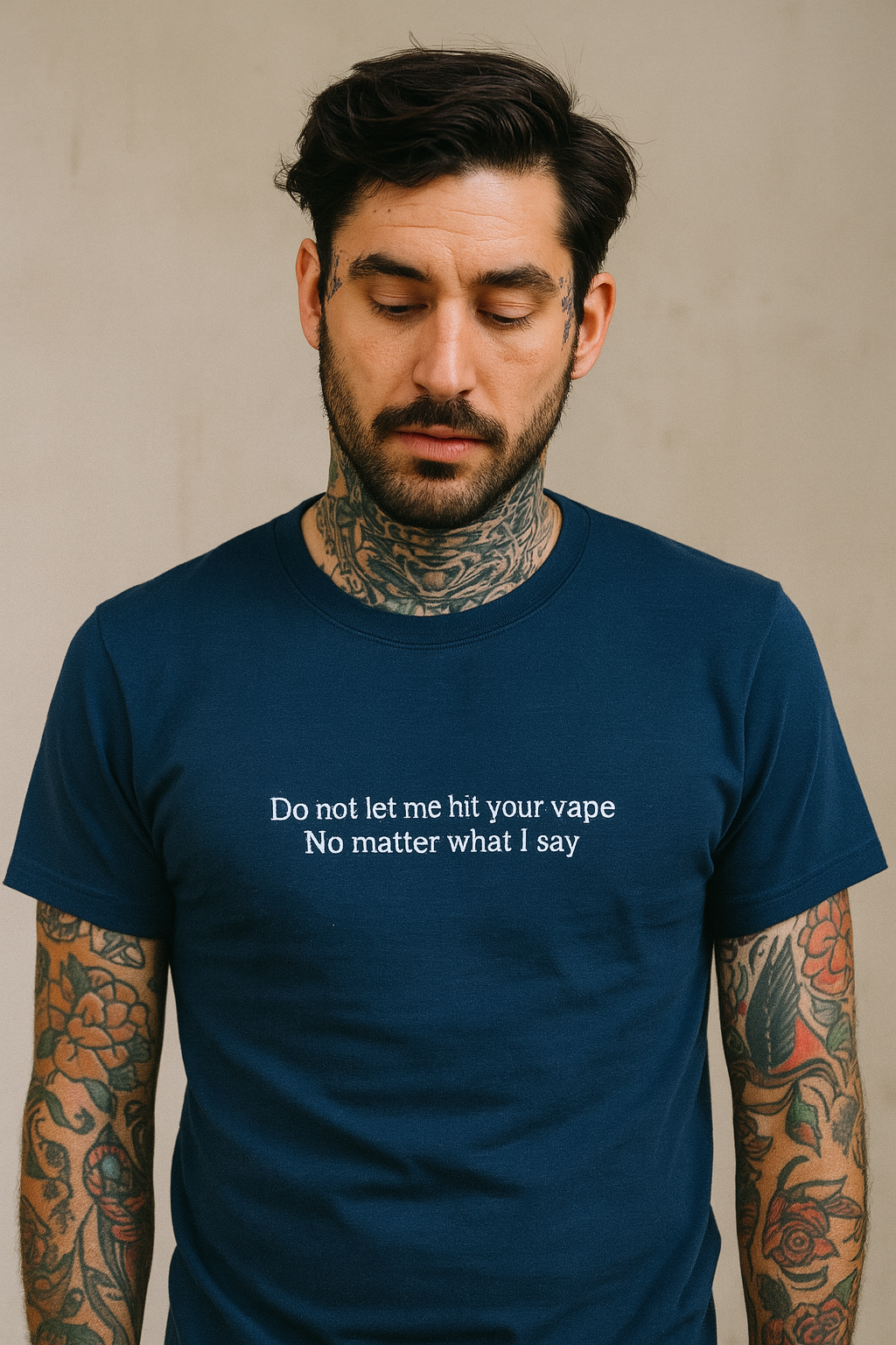 A man with tattoos on his arms wearing a blue t-shirt with a humorous message printed on it.