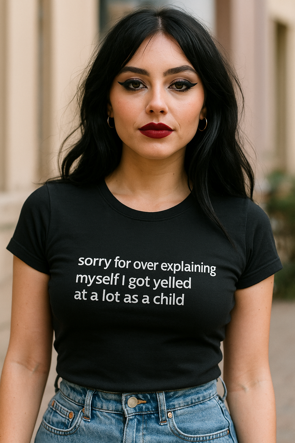 A woman with long dark hair wearing a black t-shirt with white text that says "Sorry for over explaining myself I got yelled at a lot as a child".