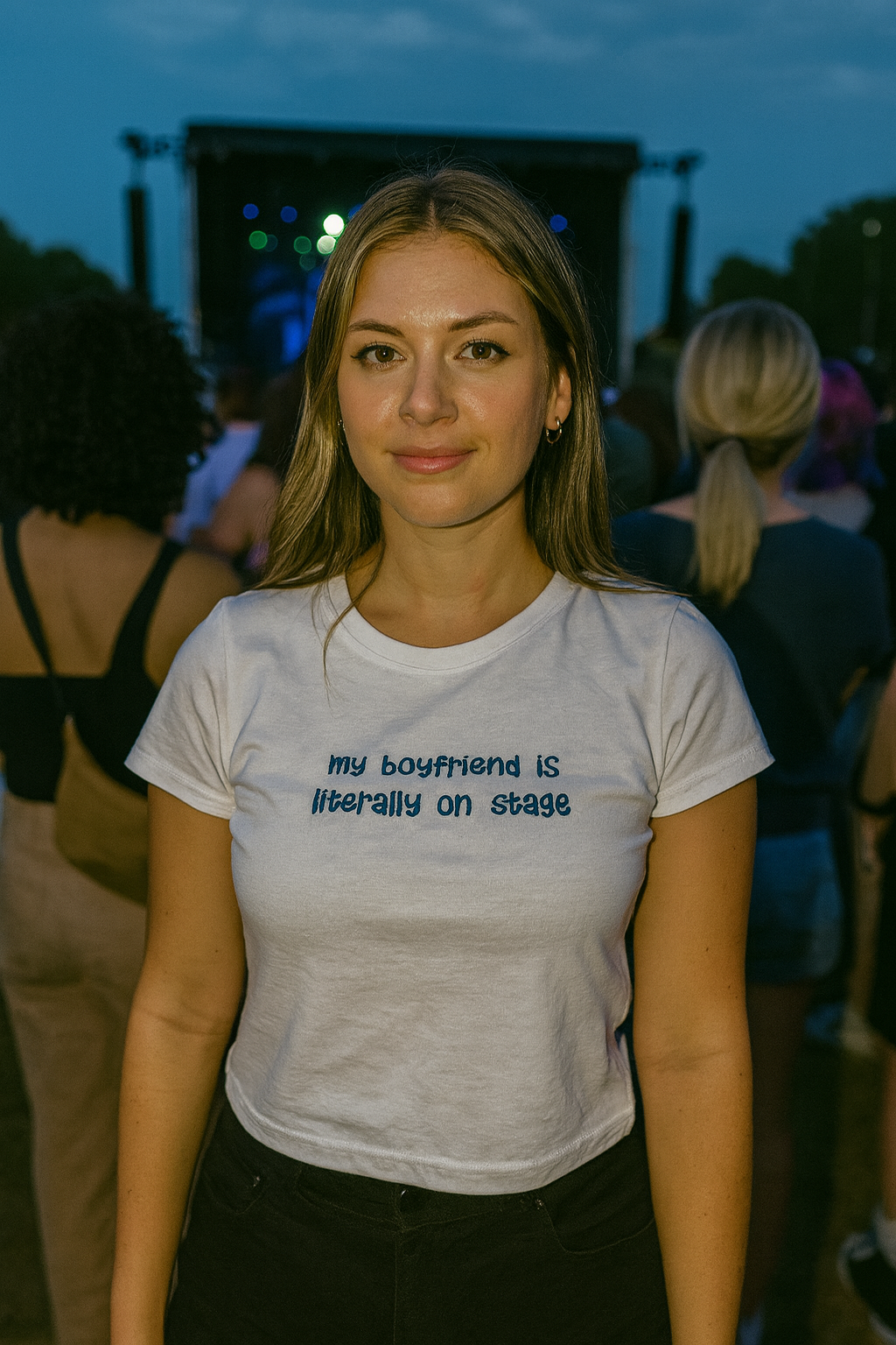 A woman wearing a white t-shirt with text stands in front of a crowd at an outdoor event.