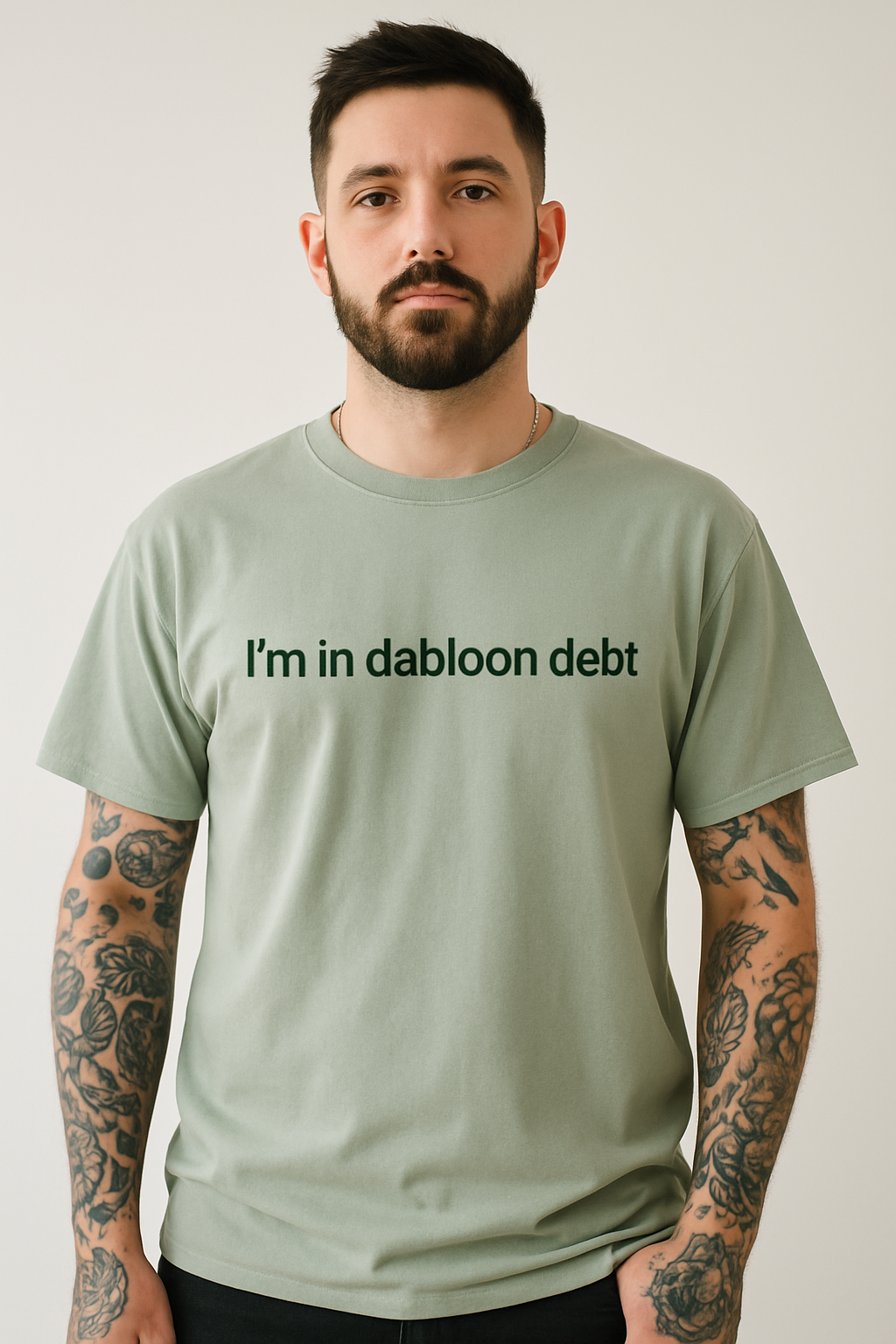A man with a beard wearing a green t-shirt with the text "I'm in dabloon debt" printed on it.