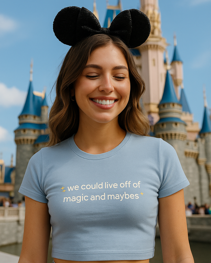 A woman wearing a blue crop top and black earrings is smiling in front of a Disney castle.