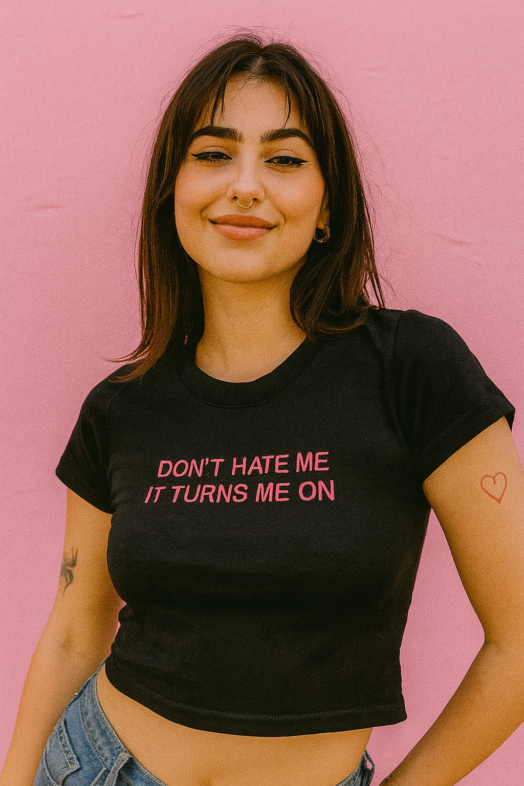 A young woman with long brown hair is smiling and wearing a black t-shirt with the text "Don't Hate Me It Turns Me On" printed on it.