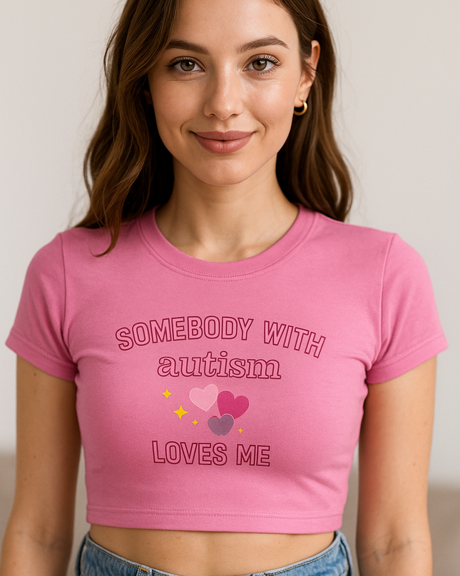 A young woman with long brown hair wearing a pink crop top with the text "SOMEBODY WITH AUTISM LOVES ME" printed on it.