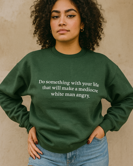 A young woman with curly hair wearing a green sweatshirt with a quote on it, standing against a beige wall.