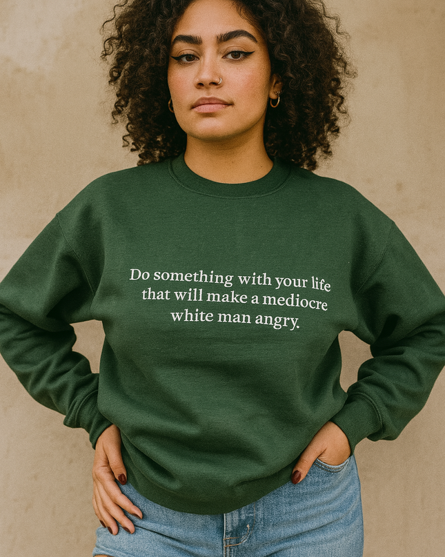 A young woman with curly hair wearing a green sweatshirt with a quote on it, standing against a beige wall.