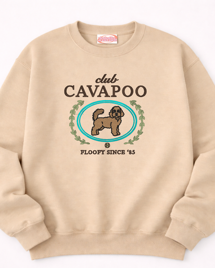 A beige sweatshirt with a graphic design featuring a dog and the text "club CAVAPOO" and "FLOOPY SINCE '85".