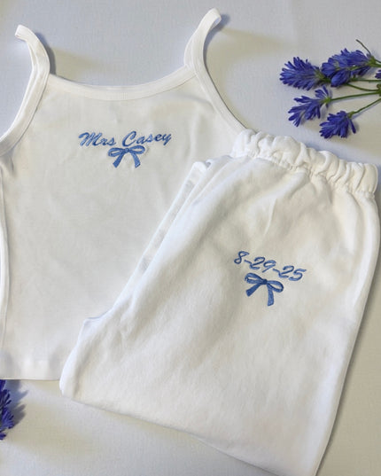 A white tank top with the name "Mrs Casey" and a pair of white pants with the date "8.29.25" embroidered on them, along with some blue flowers.