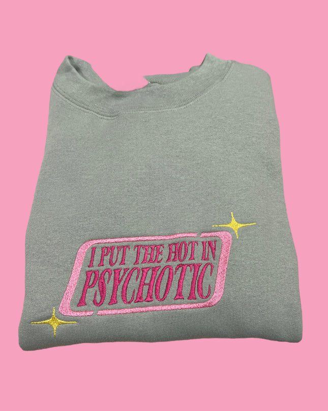 A gray sweatshirt with a pink and yellow embroidered phrase that reads "I PUT THE HOT IN PSYCHOTIC" on it.