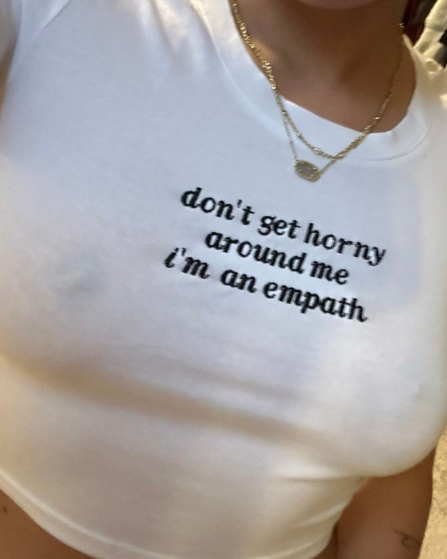 A person wearing a white t-shirt with the text "don't get horny around me I'm an empathy" printed on it.