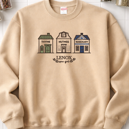 A beige sweatshirt with a graphic design depicting three houses labeled "Thyme", "Nutmeg", and "Rosemary" on a white background.