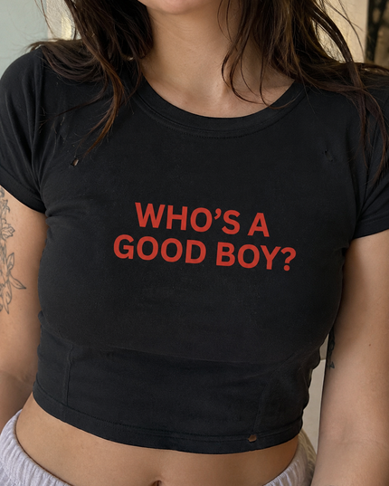 A person wearing a black crop top with the text "WHO'S A GOOD BOY?" printed on it.