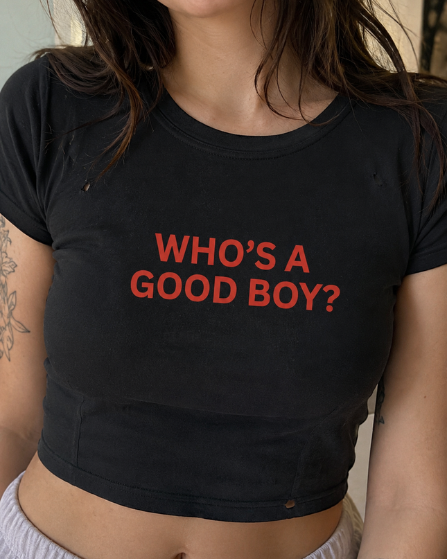 A person wearing a black crop top with the text "WHO'S A GOOD BOY?" printed on it.