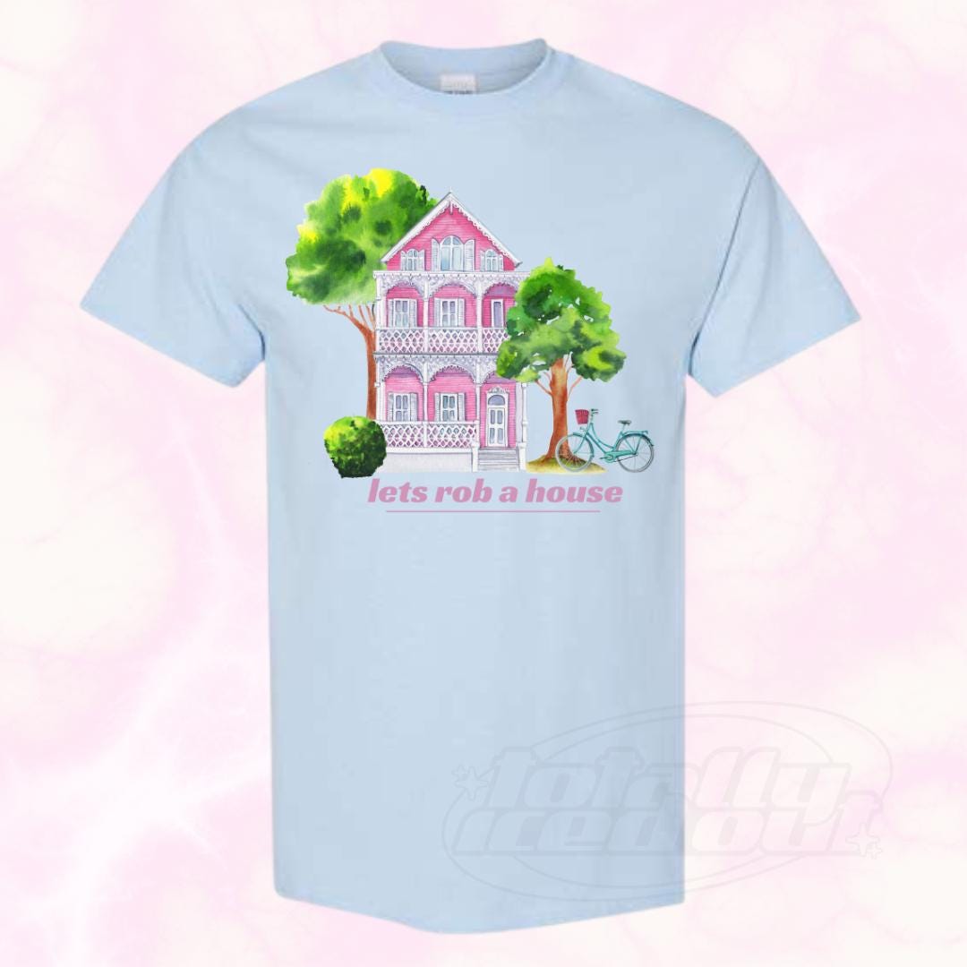 a blue t - shirt with a pink house and trees on it