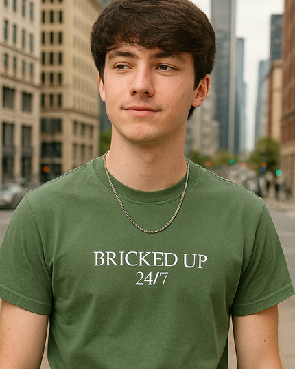 A young man wearing a green t-shirt with the text "BRICKED UP 24/7" stands in front of a cityscape with tall buildings.