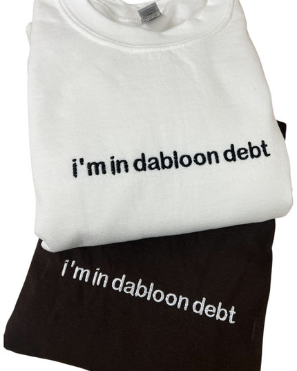 A white t-shirt with the text "i'm in dabloon debt" printed on it, and a black t-shirt underneath it.