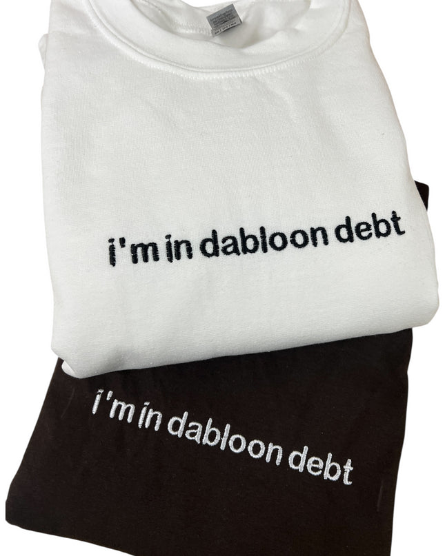 A white t-shirt with the text "i'm in dabloon debt" printed on it, and a black t-shirt underneath it.