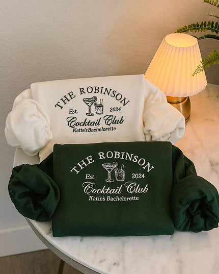 two white t-shirts with black text and logos, laid out on a white table. The t-shirts are green and appear to be related to a cocktail club or bachelorette party.