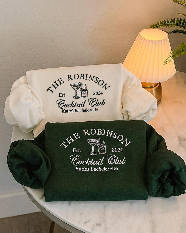 two white t-shirts with black text and logos, laid out on a white table. The t-shirts are green and appear to be related to a cocktail club or bachelorette party.