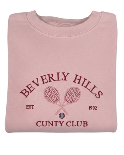 A pink sweatshirt with a graphic design featuring tennis rackets and the text "Beverly Hills Cunty Club" printed on it.