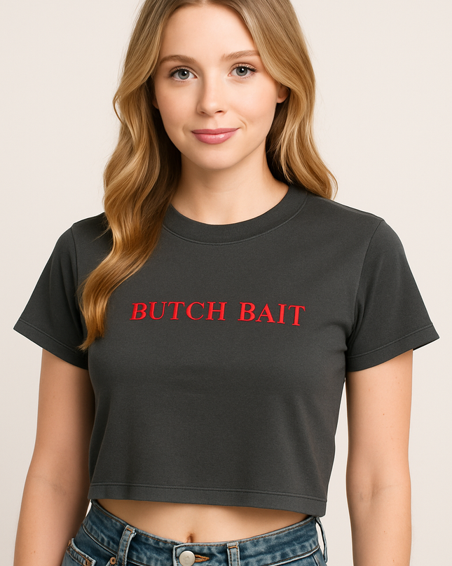 A young woman with long blonde hair wearing a black crop top with the text "BUTCH BAIT" printed on it.