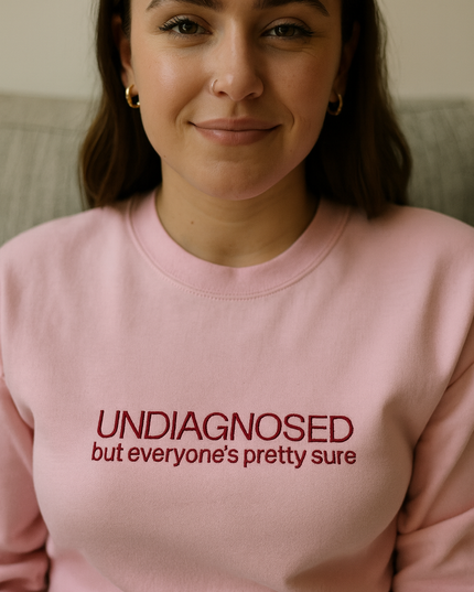 A woman wearing a pink sweatshirt with the text "UNDIAGNOSED but everyone's pretty sure" printed on it.