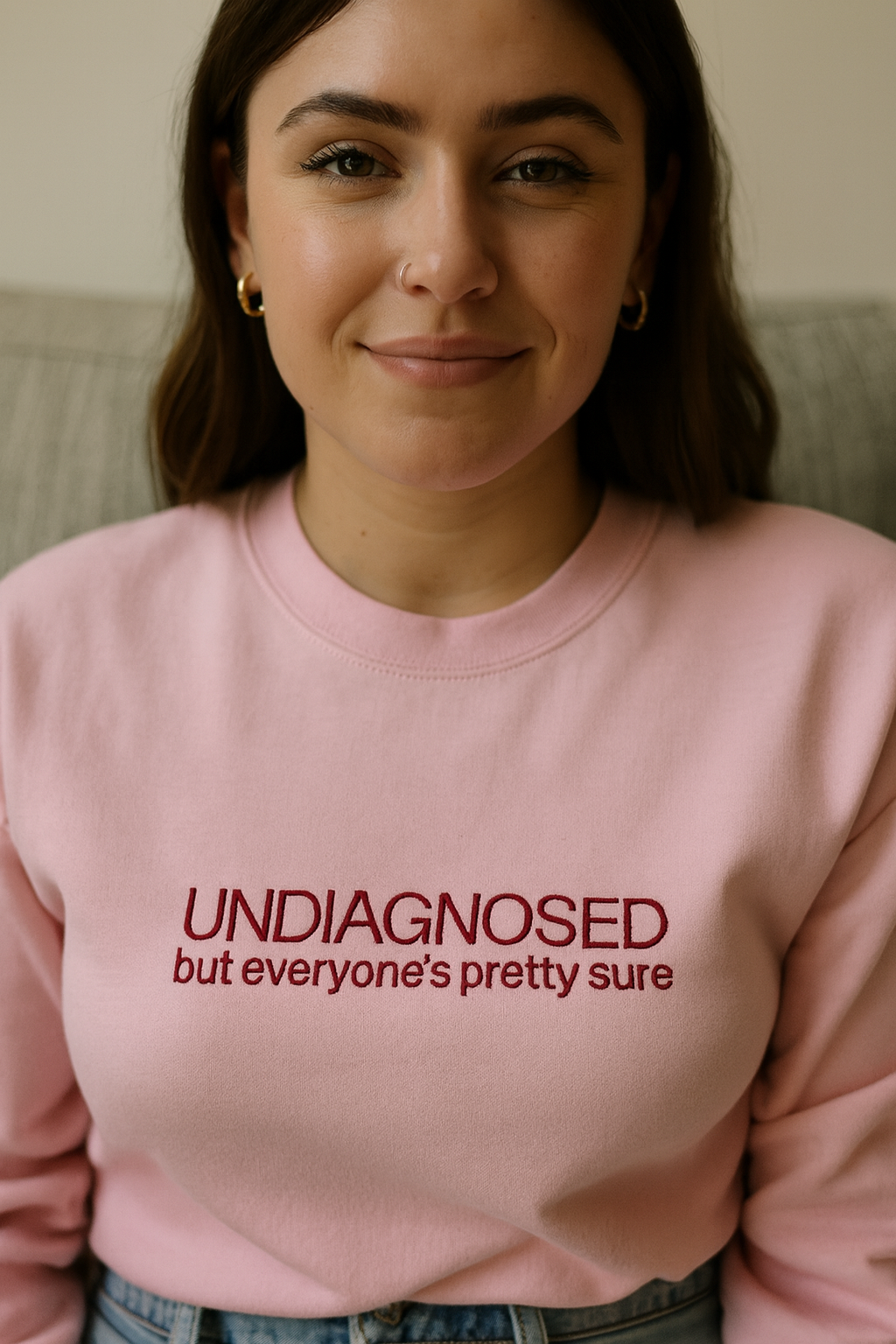 A woman wearing a pink sweatshirt with the text "UNDIAGNOSED but everyone's pretty sure" printed on it.