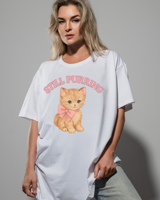 A woman wearing a white t-shirt with a graphic of a cat and the text "STILL PURRING" printed on it.