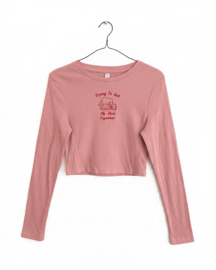 A pink long-sleeved shirt with a red graphic and text printed on it, hanging on a metal hanger.