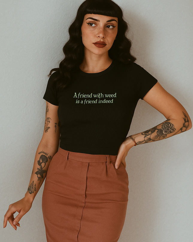 A woman with long dark hair wearing a black t-shirt with text and a brown skirt stands against a white background.