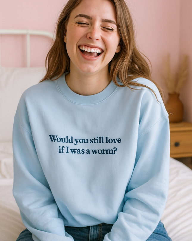 A smiling woman wearing a light blue sweatshirt with the text "Would you still love if I was a worm?"