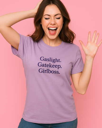 A woman wearing a purple t-shirt with the text "Gaslight. Gatekeeper. Girl boss." is smiling and waving with her hand raised.