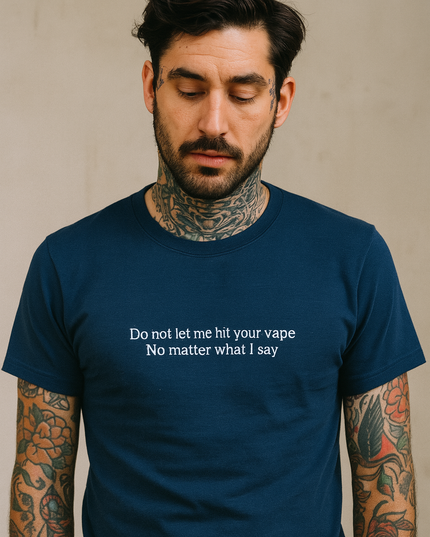 A man with tattoos on his arms wearing a blue t-shirt with a humorous message printed on it.