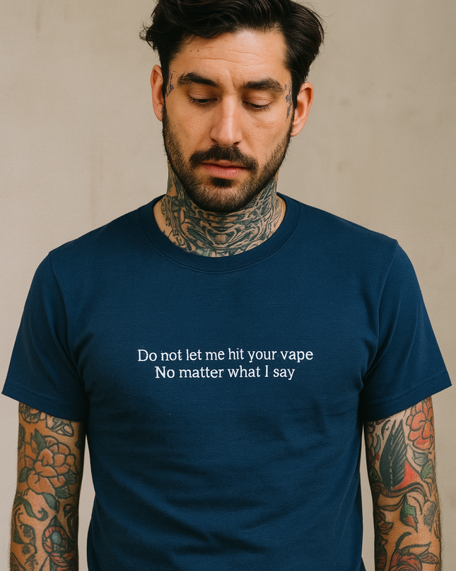 A man with tattoos on his arms wearing a blue t-shirt with a humorous message printed on it.