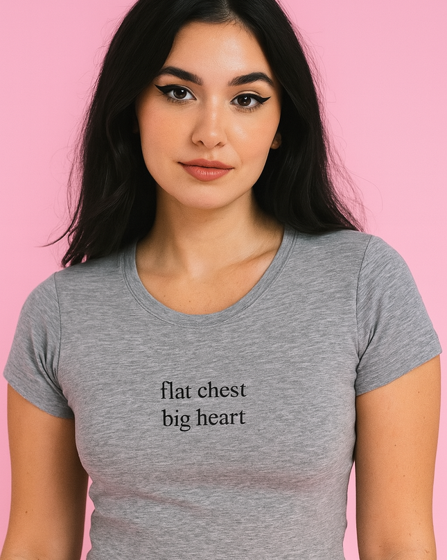 A young woman with long dark hair wearing a gray crop top with the text "flat chest big heart" printed on it.
