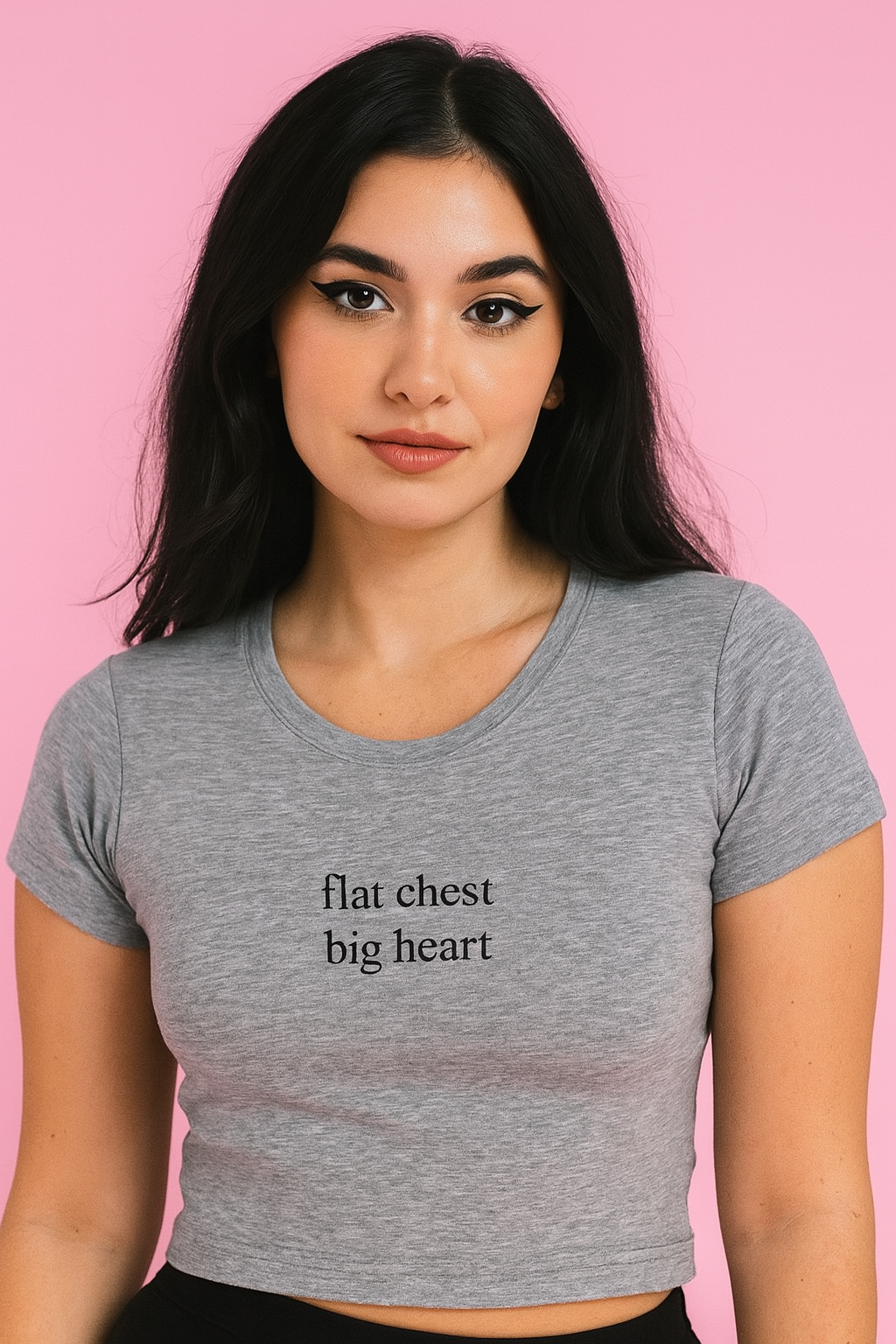 A young woman with long dark hair wearing a gray crop top with the text "flat chest big heart" printed on it.