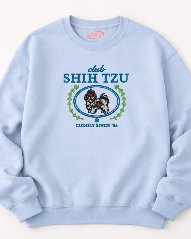 A light blue sweatshirt with a graphic design featuring a dog and the text "club SHIH Tzu Cuddly Since '85".