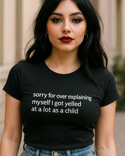 A woman with long dark hair wearing a black t-shirt with white text that says "Sorry for over explaining myself I got yelled at a lot as a child".