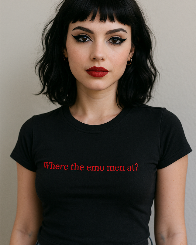 A woman with short, dark hair and bold red lipstick is wearing a black t-shirt with the text "Where the emo men at?" printed on it.