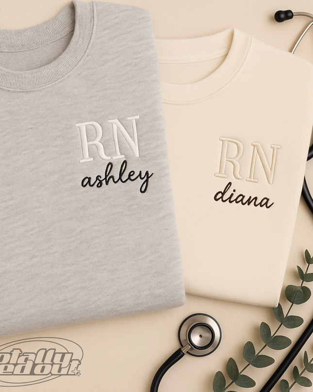 two gray sweatshirts with the initials "RN Ashley" embroidered on them, along with a stethoscope and some greenery.