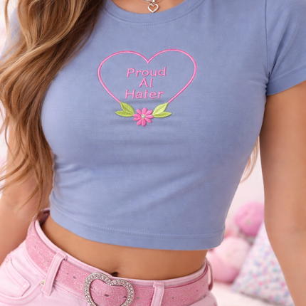 A woman wearing a blue crop top with a heart-shaped embroidered phrase and a pink belt buckle.
