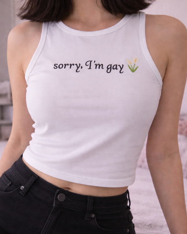 A woman wearing a white crop top with the text "Sorry, I'm gay" printed on it.