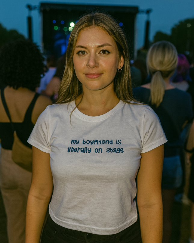 A woman wearing a white t-shirt with text stands in front of a crowd at an outdoor event.
