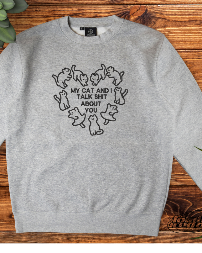 A gray sweatshirt with a black graphic design on the front, depicting a heart shape with the text "My cat and I talk shit about you" inside it.
