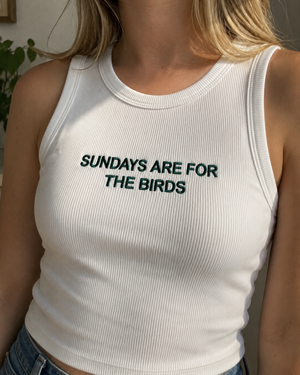 A woman wearing a white tank top with the text "SUNDAYS ARE FOR THE BIRDS" printed on it.
