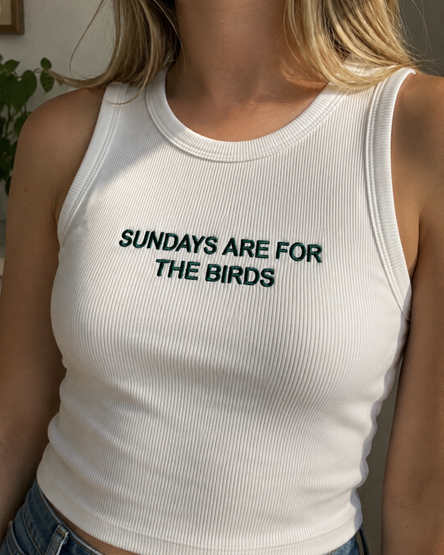 A woman wearing a white tank top with the text "SUNDAYS ARE FOR THE BIRDS" printed on it.