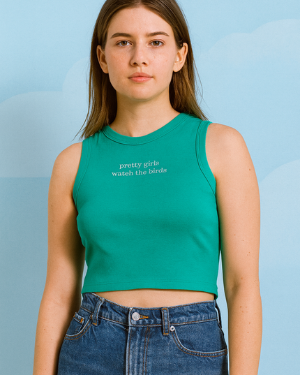 A young woman wearing a green crop top and blue jeans stands against a blue sky background.